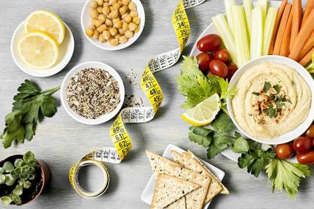 Vu du dessus : une table sur laquelle est posée un assiette de crudités un ruban de mesure et des petits contenants de légumineuses.