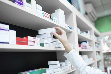 La main d'un pharmacien attrapant une boite de médicament sur les étagères de l'officine.